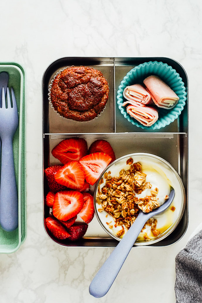 Yogurt lunch: plain yogurt with honey and granola, strawberries on the side, rolled up ham, and a muffin in a bento box.