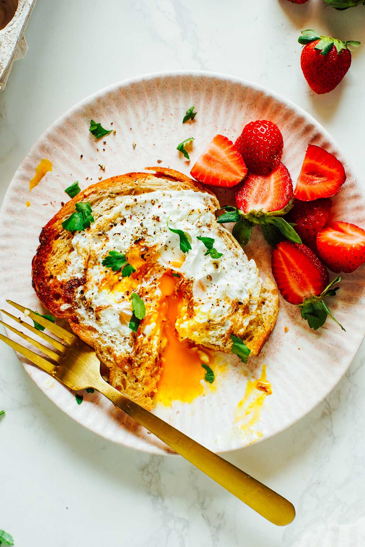 Egg cooked inside a piece of buttery toast on a pink plate with strawberries.