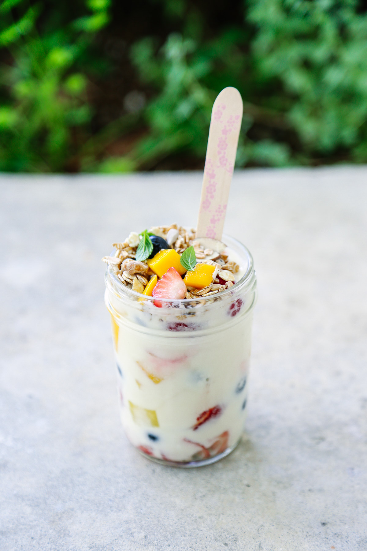 Fruit and yogurt parfait in a mason jar topped with granola and mango chunks.
