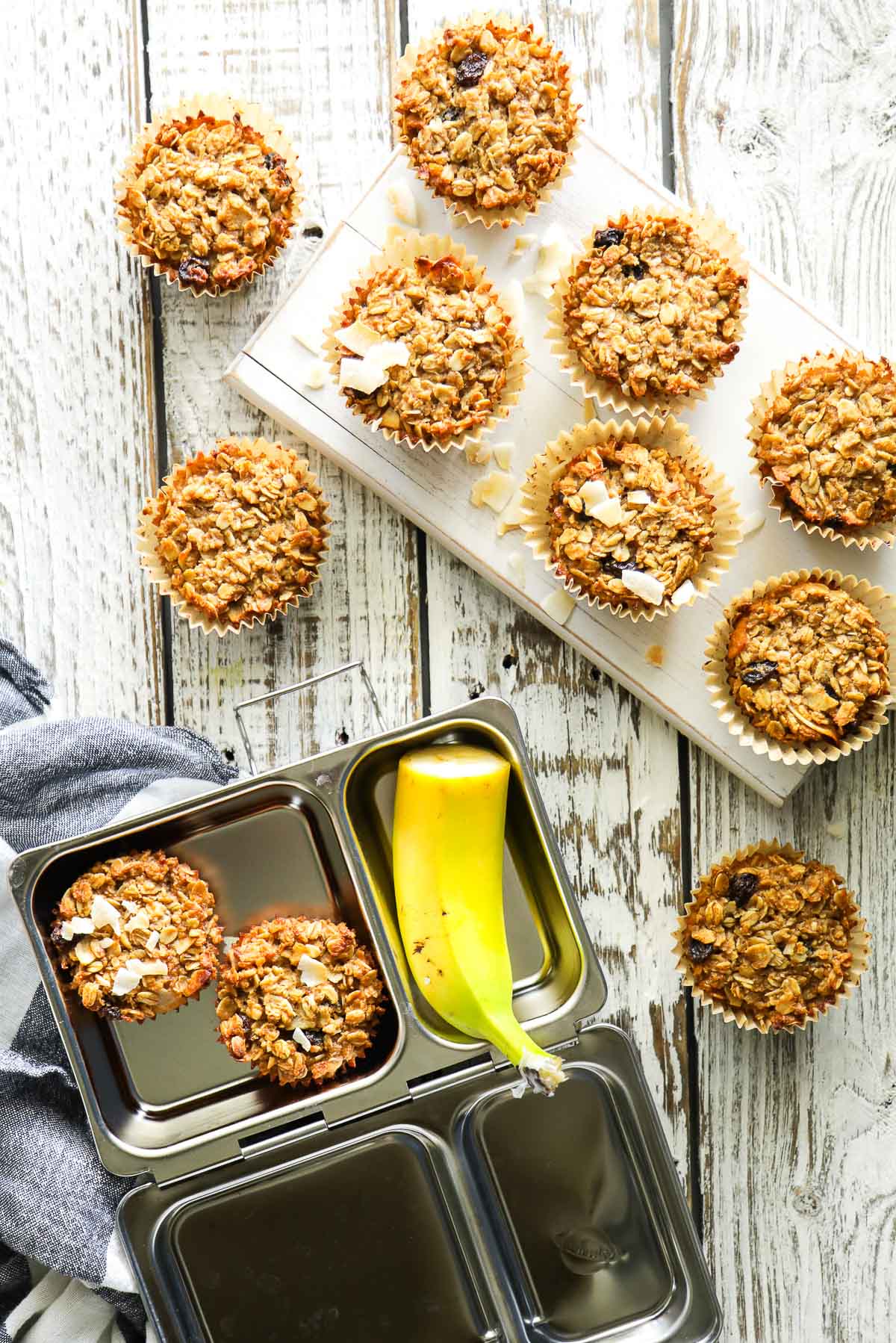 Baked oatmeal cups on a cutting board and lunchbox with a banana on the side.