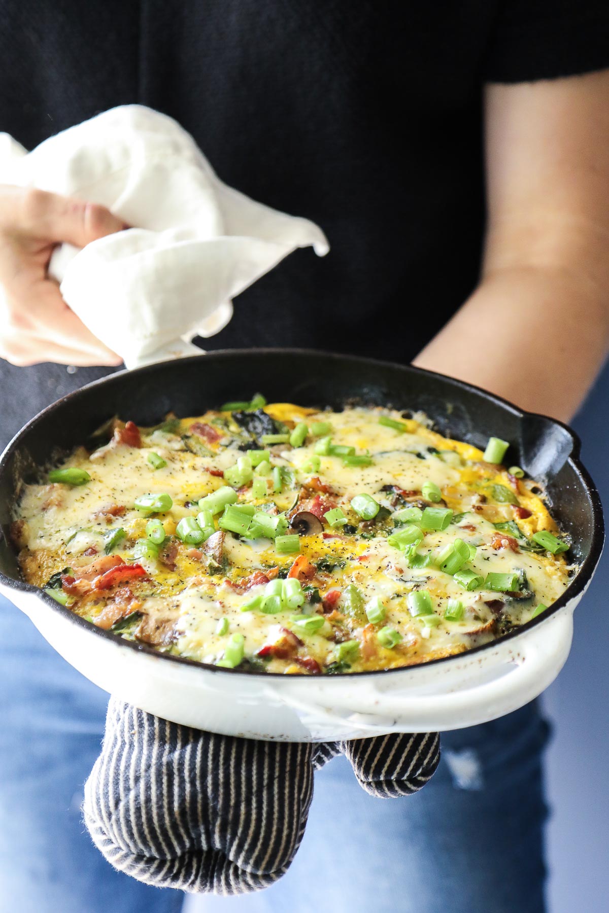 Hands holding a cast iron skillet with a veggie frittata baked inside.