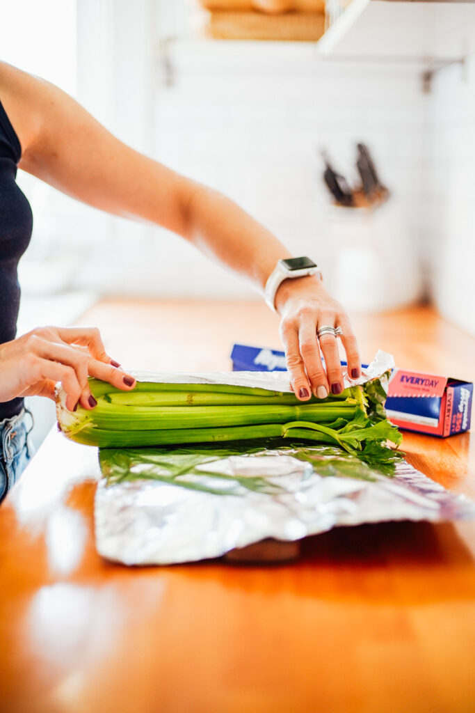 Placing a whole celery in a piece of foil for storage.