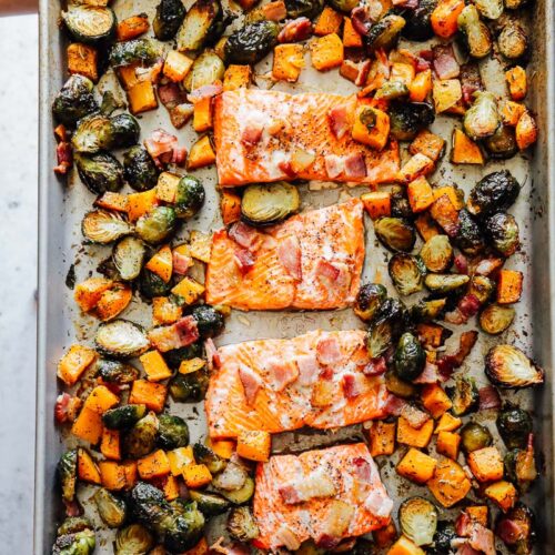 Roasted veggies pushed to the side of the sheet pan with cooked salmon in the center topped with bacon.