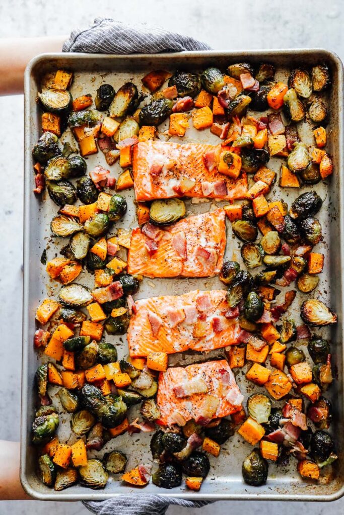 Roasted veggies pushed to the side of the sheet pan with cooked salmon in the center topped with bacon.