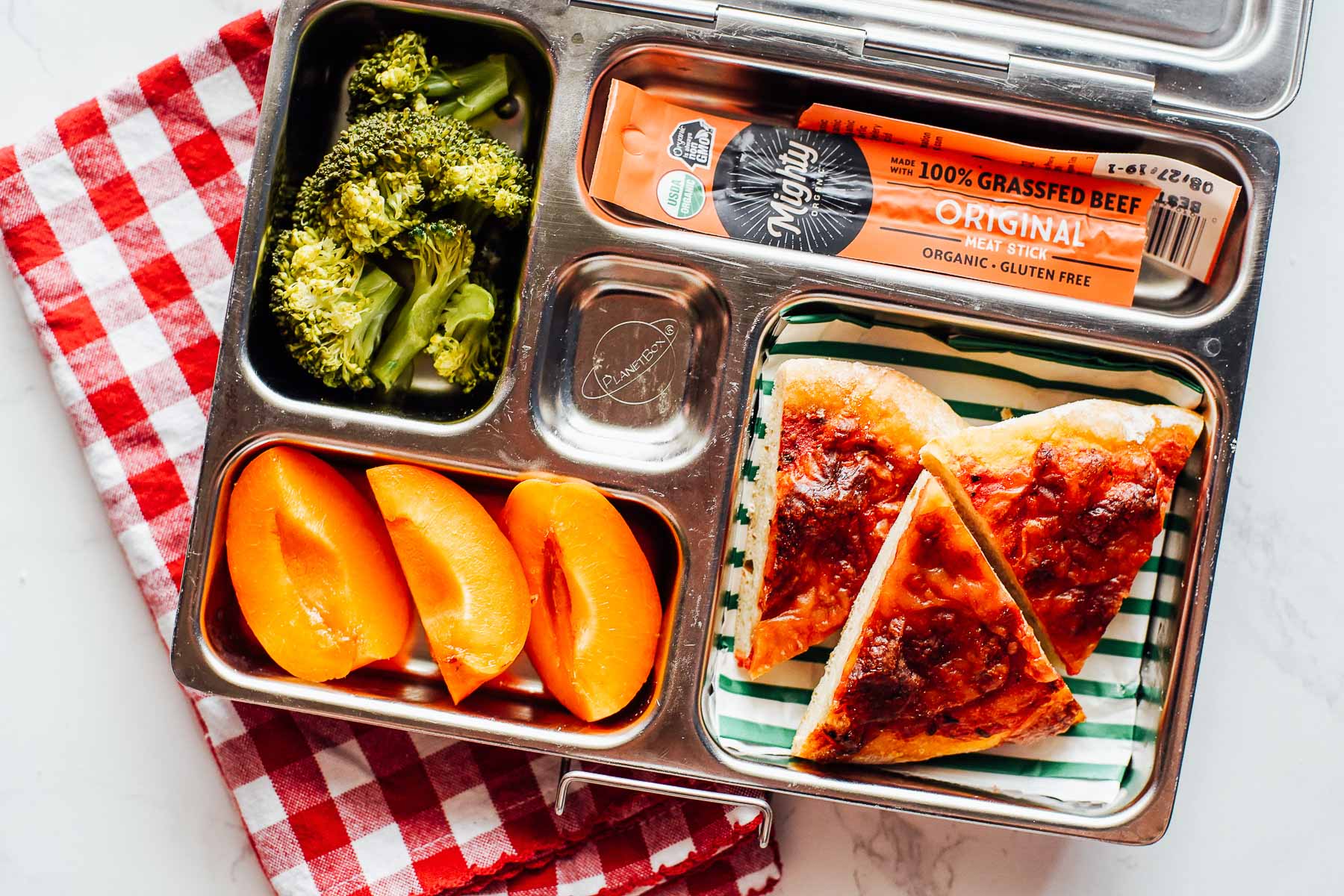 Lunchbox meal: pizza, apricots, roasted broccoli, meat jerky stick.